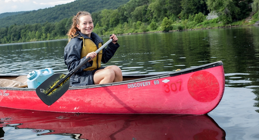 A person wearing a lifejacket paddles a red canoe on calm water